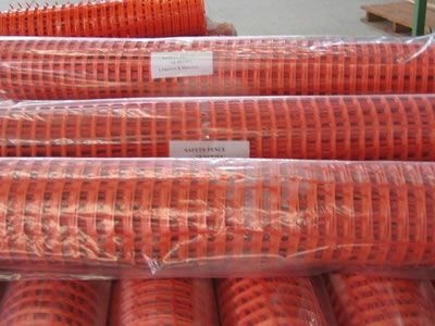 Rolls of orange construction fence are covered by plastic film bags.